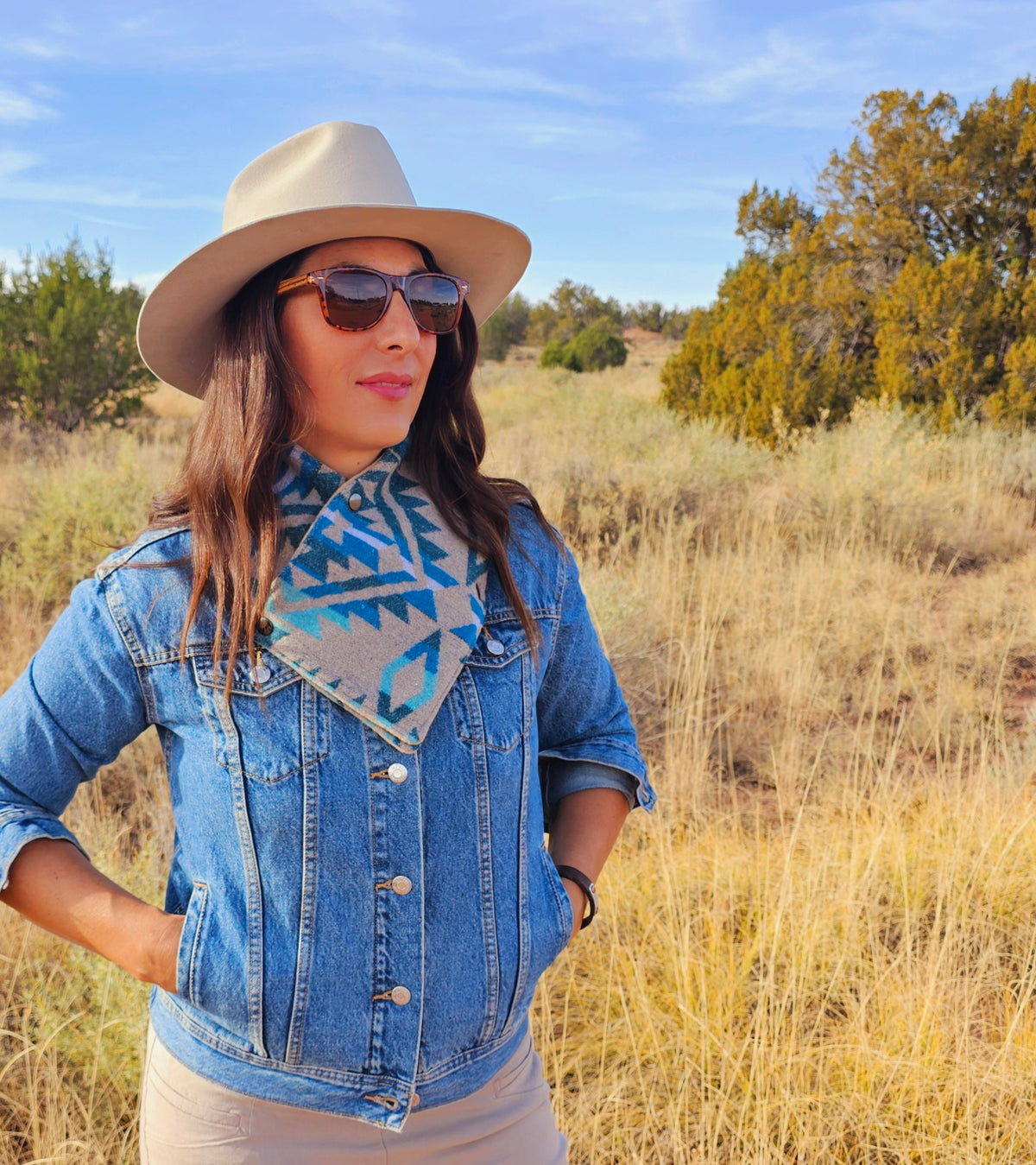 Woman wearing the Turquoise/Tan Aztec cowl, denim jacket and hat outdoors in a sunlit field.