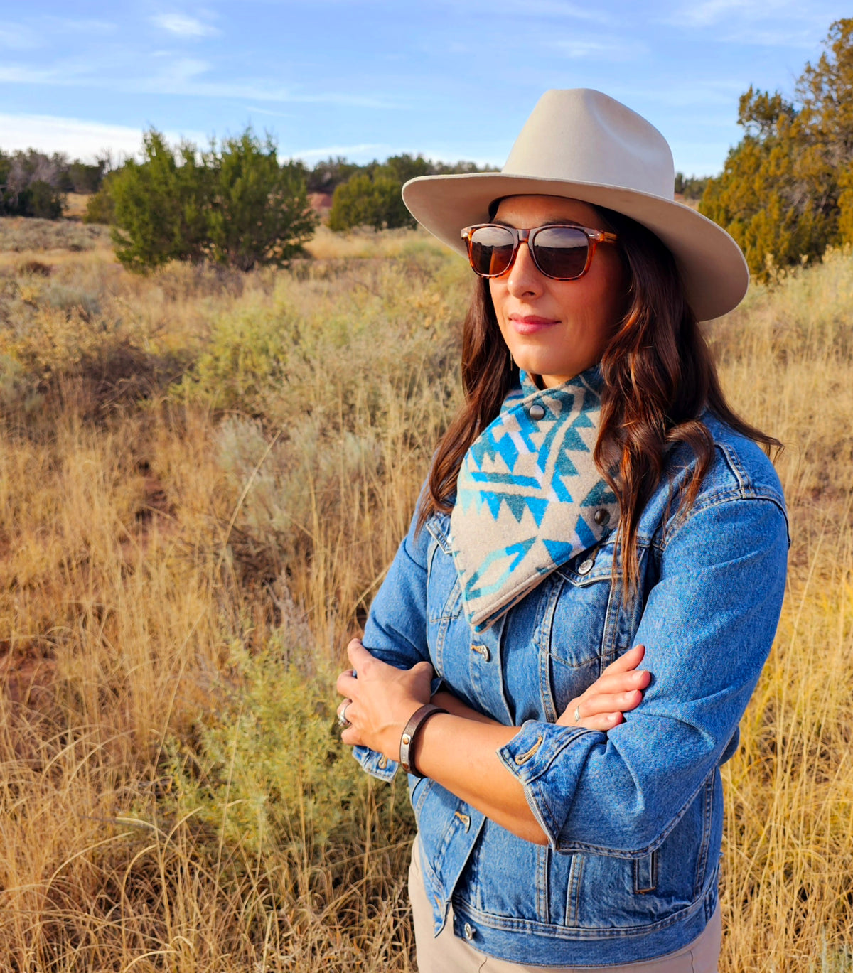 Woman wearing the Turquoise/Tan Aztec cowl with a denim jacket and wide-brimmed hat in a grassy landscape.