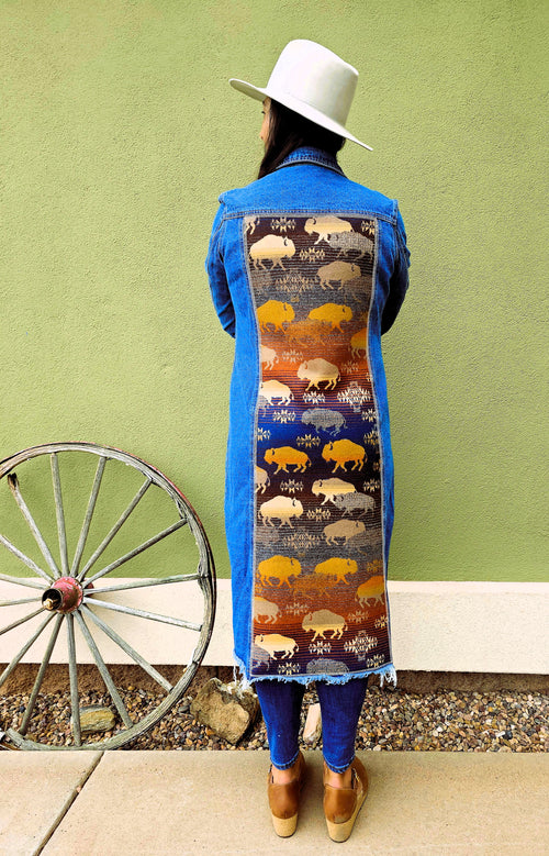 Back view of a woman wearing the long Land of the Buffalo denim duster with a full-length buffalo-patterned wool panel.