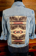 Back of a light-wash denim jacket with a large brown, cream, red, and turquoise geometric wool panel.