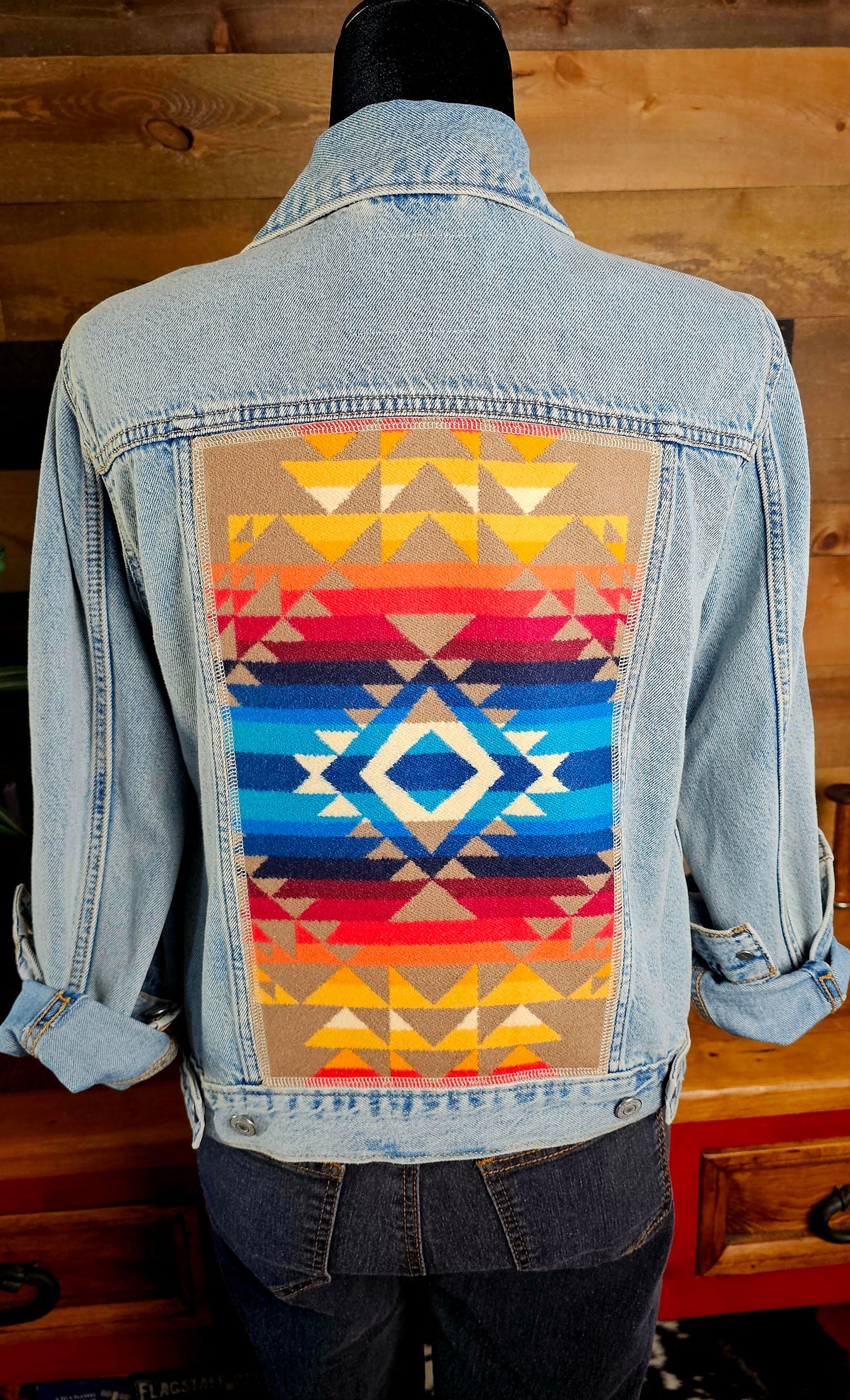 Pilot Rock denim jacket on a mannequin, showing its blue diamond and red-and-gold geometric wool back panel.