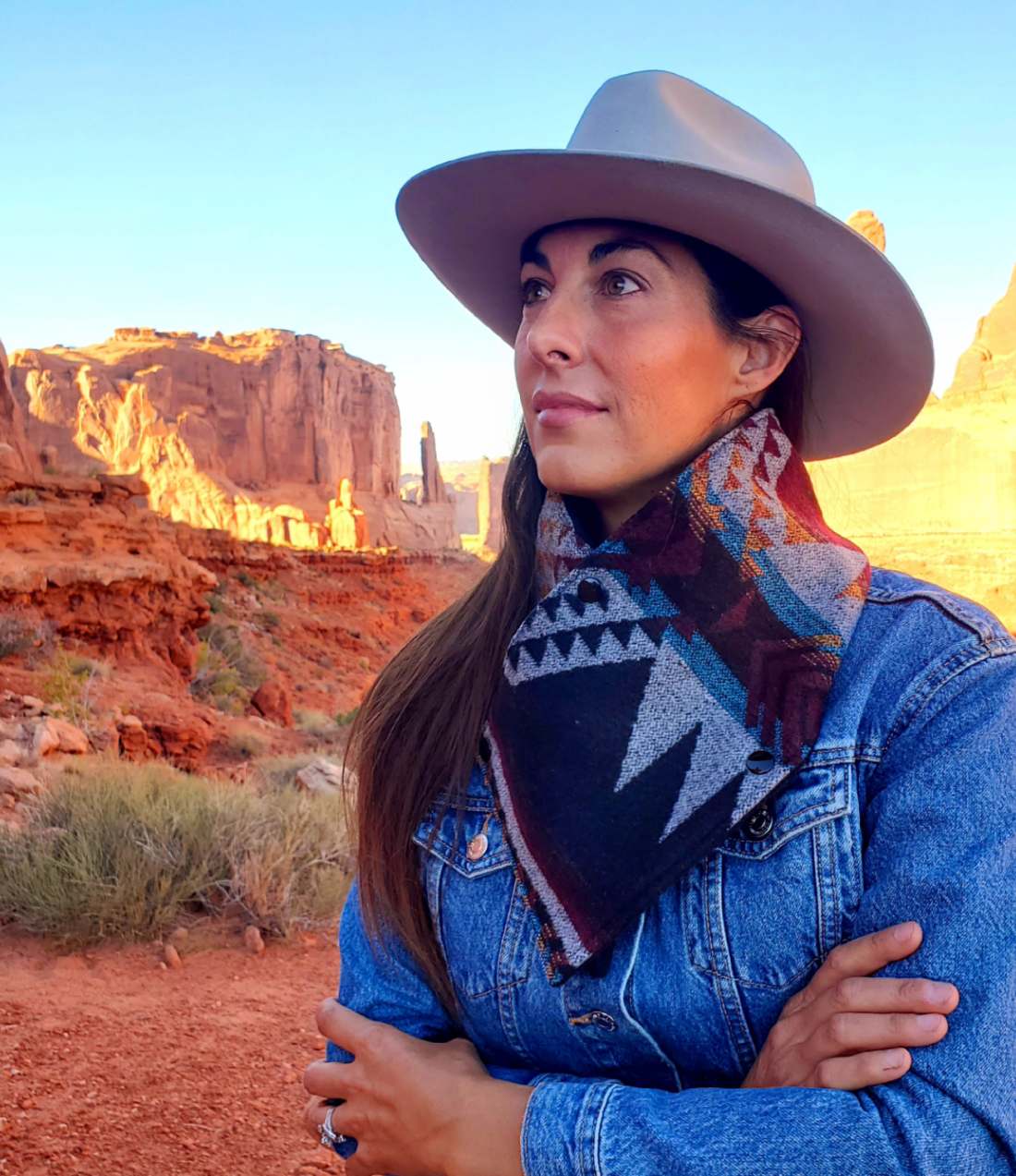 Woman wearing a patterned wool cowl and wide-brimmed hat in a red-rock canyon.