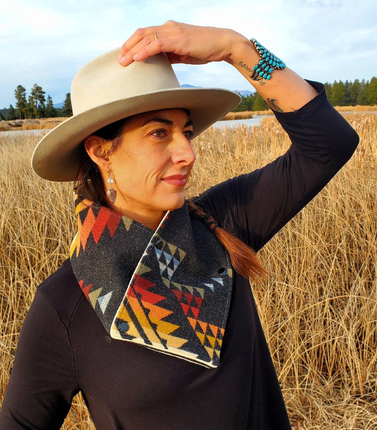 Western cowl neck scarf is displayed on model standing in wetland & looks similar to bandana. Made with Pendleton® blanket-weight wool, the design features black, red, tan, blue, green geometric shapes that are popular in the Southwest.