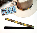 Monster Brown trout hat band folded beside a light hat and fishing fly box, showing the patterned front and dark backing.
