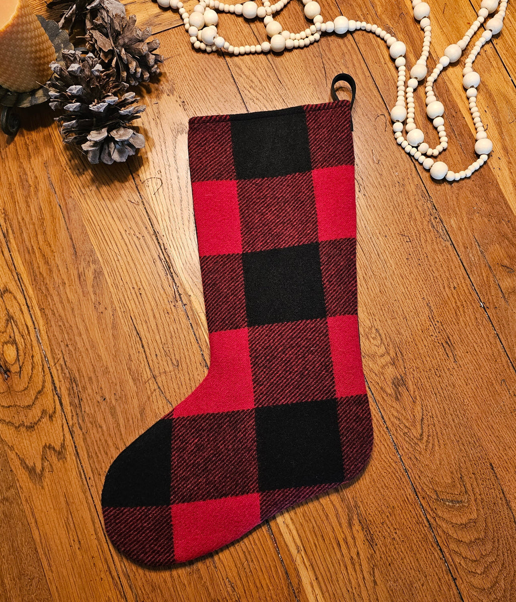 Front of a red and black buffalo check Christmas stocking displayed flat on a wooden surface.
