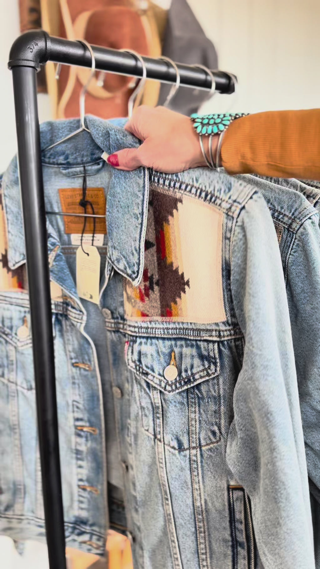 Denim jackets with geometric wool panels displayed on a clothing rack.