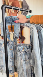 Denim jackets with geometric wool panels displayed on a clothing rack.