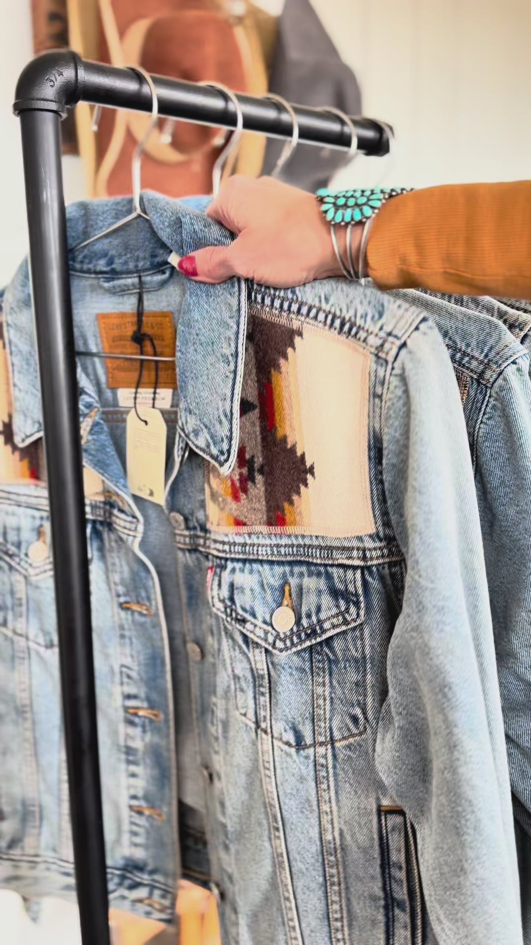 Denim jackets with geometric wool panels displayed on a clothing rack.