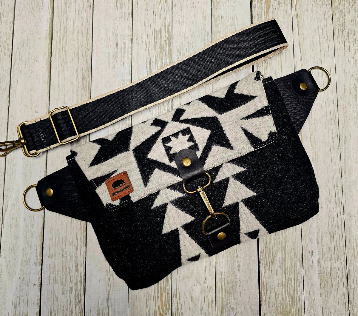 Condensed White sling laid flat with its black strap and large cream geometric motif visible.