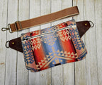 Back view of the Canyonlands sling laid flat with red and blue patterned fabric and a brown strap.