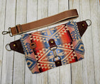 Canyonlands sling laid flat, showing its colorful geometric pattern, exterior zipper and brown strap.
