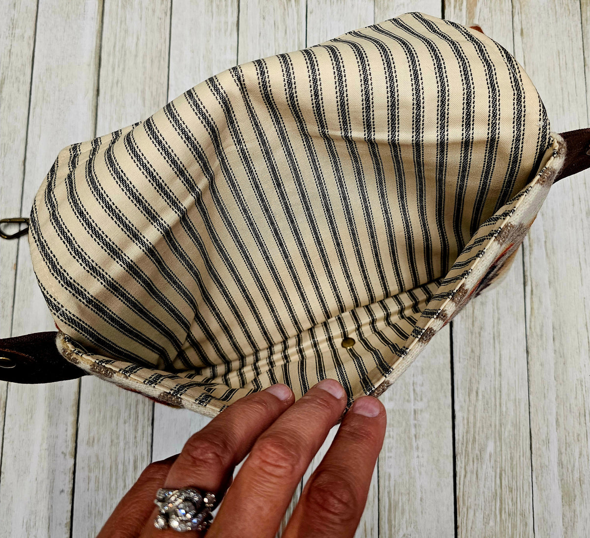Open Condensed White sling showing its striped fabric lining and interior compartment.